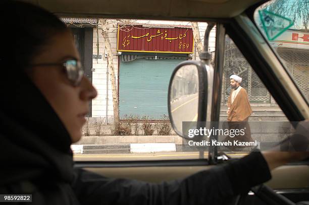 Woman driving a car in south Tehran, drives past a cleric attending The Day of Ashura ceremony which is on the 10th day of Muharram in the Islamic...