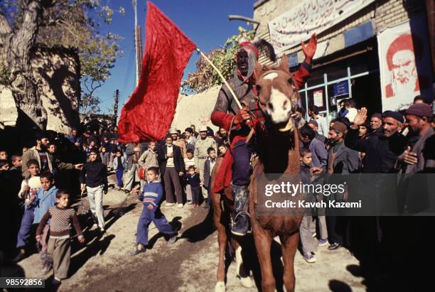 Man dressed as Shemr the man who cut off Imam Hussein's head, rides on a horse, passing villager onlookers during Ta'zieh on The Day of Ashura in a...