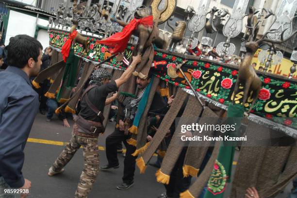 Man carries an Alam is helped by fellow mourners to keep his balance, also to keep people out of danger of collision while he spins around, outside a...