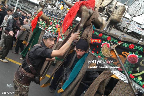 Man carries an Alam is helped by fellow mourners to keep his balance, also to keep people out of danger of collision while he spins around, outside a...