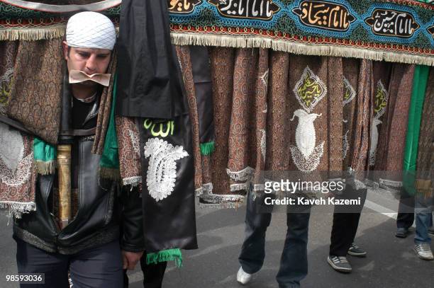 Man with a banknote stuck in his mouth by spectators, carries an Alam , while on march, outside a mosque on The Day of Ashura in south Tehran. Ashura...