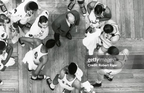 Overhead view as head coach Red Auerbach of the Boston Celtics talks to his players during a game, circa 1960s.