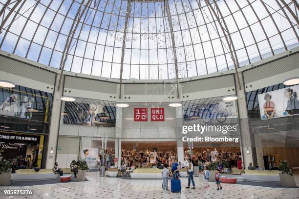 Uniqlo store, operated by Fast Retailing Co., center, and other clothing outlets stand under a glass domed ceiling inside the Val d'Europe shopping...