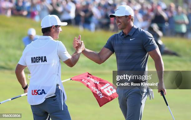 Brooks Koepka of the United States celebrates with caddie Richard Elliott on the 18th green during the final round of the 2018 U.S. Open at...