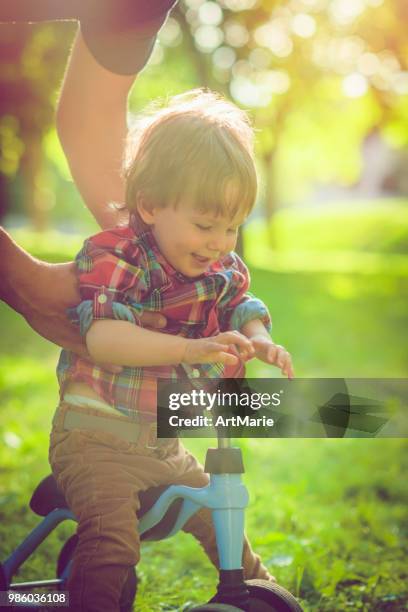 father and his son on a runbike in summer park - artmarie stock pictures, royalty-free photos & images