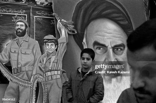 Young boy stands in front of a portrait of Ayatollah Khomeini and a cut out figure of two Basiji combatants around the Tehran university, 30th...