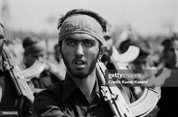 Young Basiji man carrying an AK-47 and wearing a headband with Islamic slogan marches on the anniversary of the Iran-Iraq war in Azadi square in...