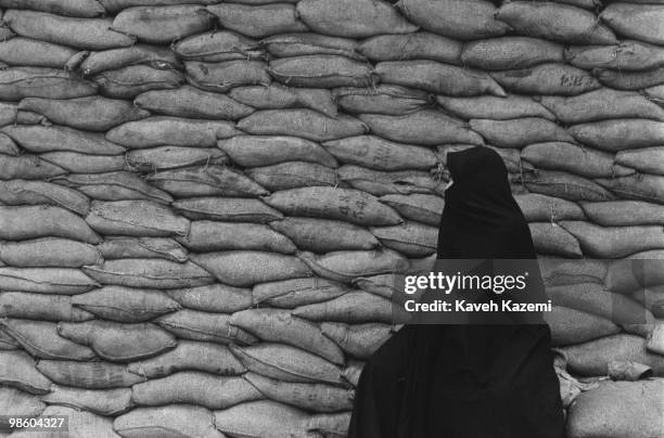 Woman in black chador sits on sandbags piled up for air raid shelter, 11th May 1988. Towards the end of the eight year-long Iran-Iraq war, Iraq was...