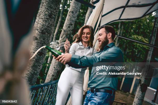 cute couple opening champagne bottle for their anniversary party - drunk husband stock pictures, royalty-free photos & images