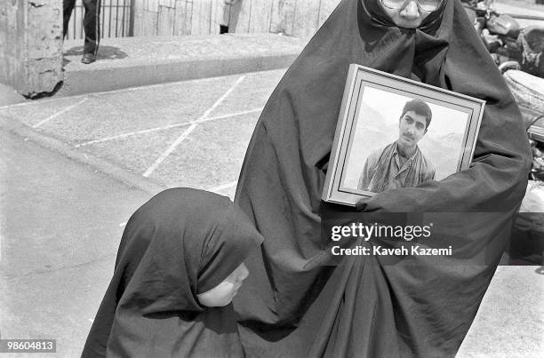 Mother of young martyr of revolutionary forces killed Iran - Iraq war, holds picture of her son in Behesht-e Zahra ceremony, Tehran.