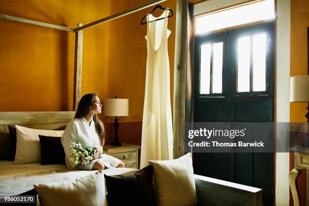 Bride sitting on bed in hotel room with eyes closed before wedding