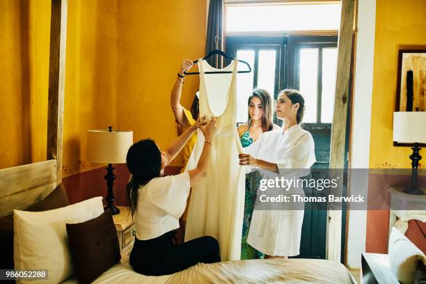 Women in bridal party admiring wedding dress with bride in hotel room before ceremony