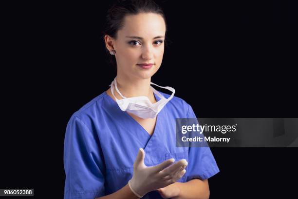 portrait of young female doctor, wearing a blue scrubs and a surgical mask and putting on her protective gloves, in front of black background. - executivo chefe de operações - fotografias e filmes do acervo