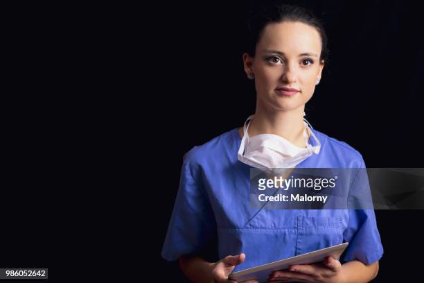 portrait of young female doctor, wearing a blue scrubs and a surgical mask and holding a digital tablet, in front of black background. - executivo chefe de operações - fotografias e filmes do acervo