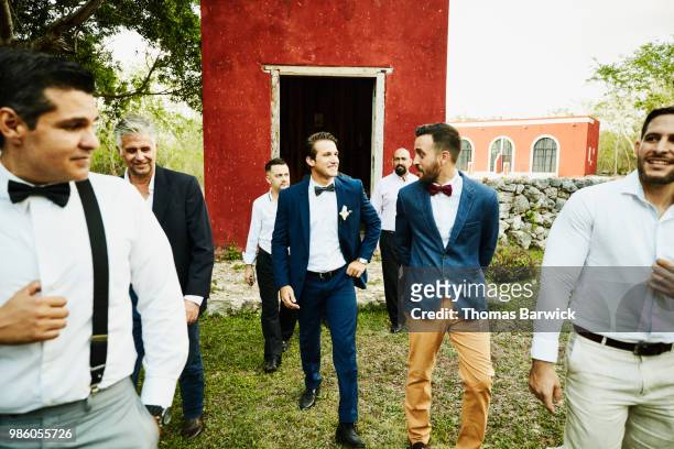 Smiling men in wedding party walking to reception after having photo taken in front of chapel