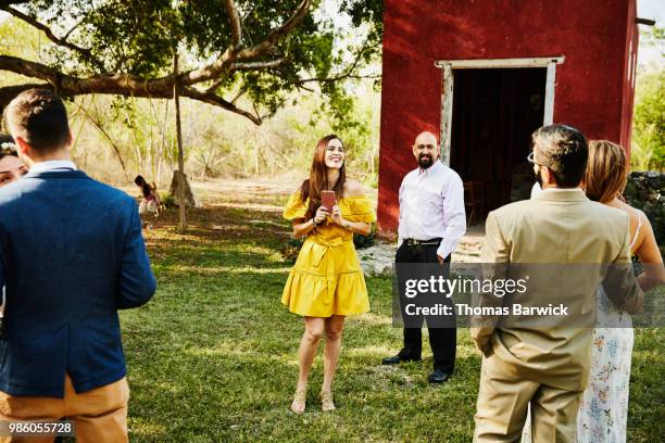 laughing woman sticking her tongue out after taking photos of wedding guests with smartphone during outdoor reception - wedding party stock pictures, royalty-free photos & images