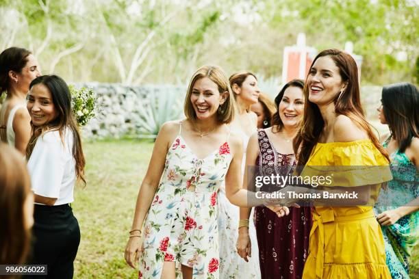 laughing female friends in discussion during outdoor wedding reception - jurk stockfoto's en -beelden