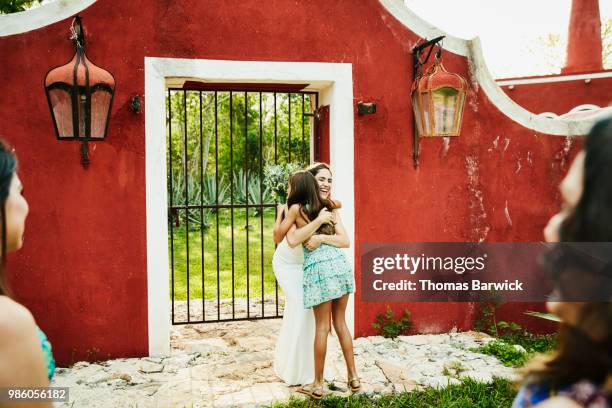 smiling bride hugging young niece after catching bouquet during outdoor wedding reception - red dress child stock pictures, royalty-free photos & images