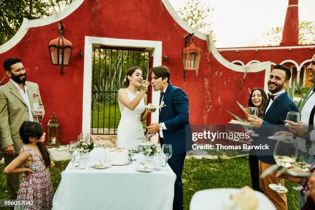 laughing bride feeding cake to groom during outdoor wedding reception - destination wedding imagens e fotografias de stock