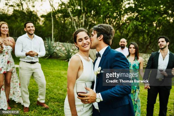 Groom kissing bride on cheek during wedding reception at tropical resort