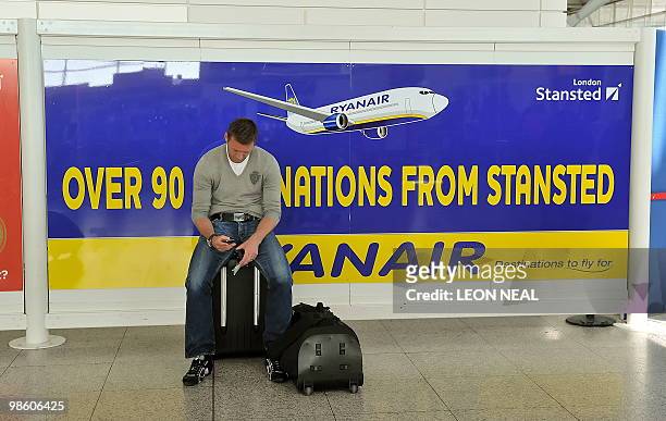 Man sits on his luggage beside an advert for Irish low-cost airline Ryanair in the departures area of Stansted airport in Essex, on April 22, 2010....