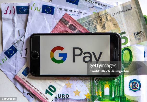 Symbol photo on the topic pay with the smartphone. The picture shows the G Pay logo on a smartphone display. The smartphone lies on euro banknotes.