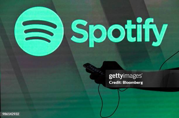 Man checks his smartphone whilst standing amongst illuminated screens bearing the Spotify Technology SA logo in this arranged photograph in London,...