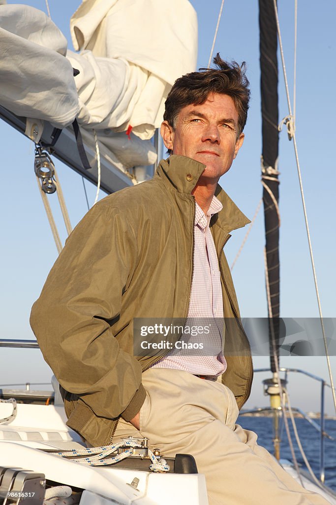 Active man relaxing on deck of sailboat at sunset.