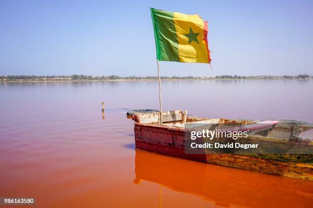 Boat with a Senegalese flag floats on Lac Rose on the edge of Dakar, Senegal. Lac Rose is a saline lake that gets its color from a special type of...