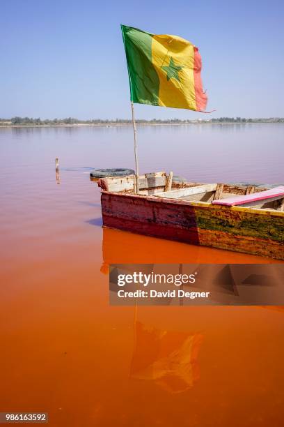 Boat with a Senegalese flag floats on Lac Rose on the edge of Dakar, Senegal. Lac Rose is a saline lake that gets its color from a special type of...