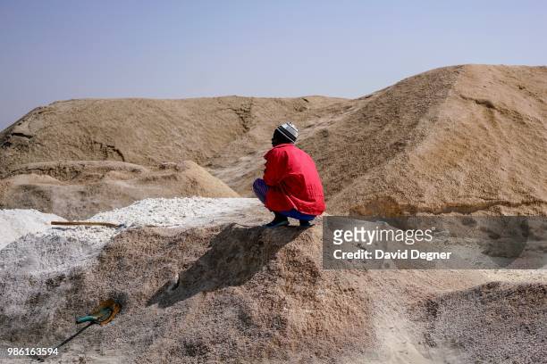 Man sits on a pile of sand beside Lac Rose on the edge of Dakar, Senegal. Lac Rose is a saline lake that gets its color from a special type of algae...