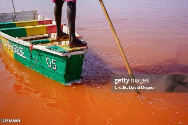 Boat is pushed through the water of Lac Rose on the edge of Dakar, Senegal. Lac Rose is a saline lake that gets its color from a special type of...