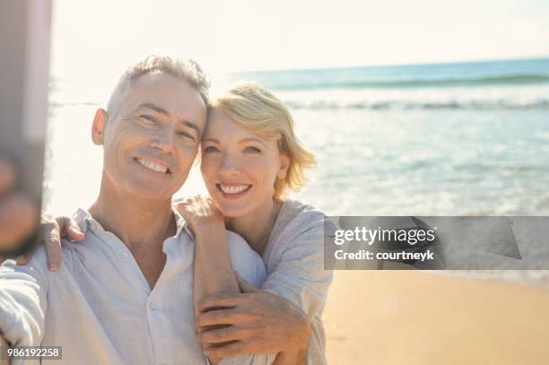 älteres paar unter einem selfie am strand mit einem mobiltelefon. - the face of australia photo call stock-fotos und bilder