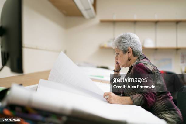 senior silver-haired woman, engeneer, measuring the space on the drawing of architectural project with curvimeter. - alex potemkin or krakozawr stock pictures, royalty-free photos & images