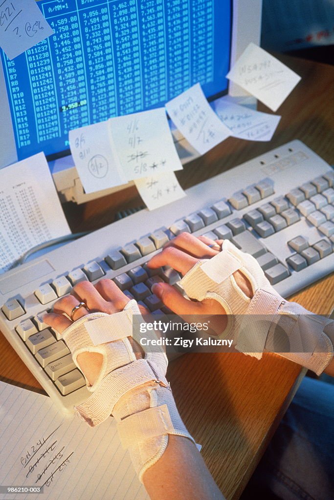 Hands wearing braces, typing at keyboard (carpal tunnel syndrome)