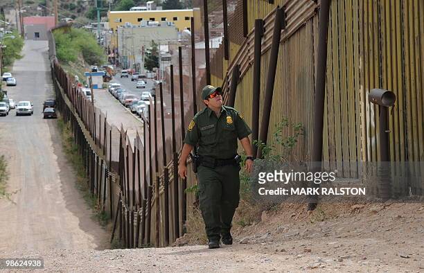 Border Patrol officers walks beside the border fence that divides the US from Mexico in the town of Nogales, Arizona on April 22, 2010. Two...