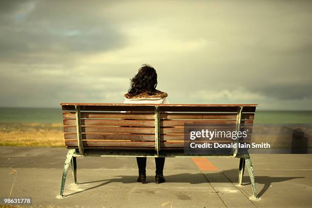 woman watches the ocean sitting on bench - bench sea stock-fotos und bilder