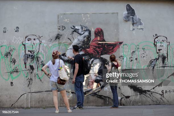 People look at a recent artwork by anonymous street artist Banksy in Paris, on June 28, 2018. - Following mutiple detorations of Banksy's work this...