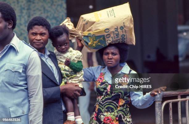 Femme portant un sac sur la tête accompagnée d'un homme portant son enfant à Nairobi en juillet 1978, Kenya.