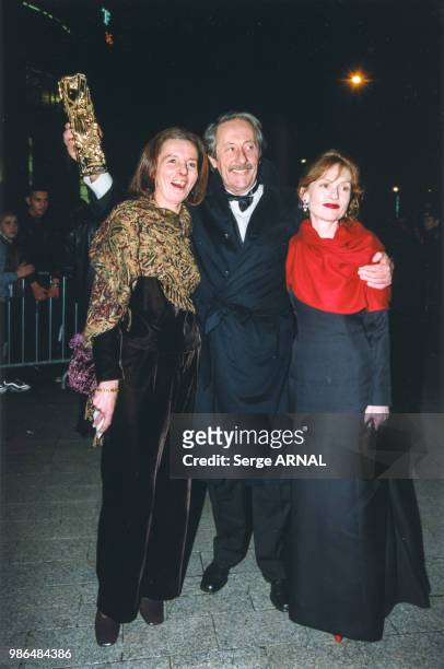 Jean Rochefort brandissant son César entouré de sa femme et d'Isabelle Huppert après la cérémonie le 6 mars 1999 à Paris, France.