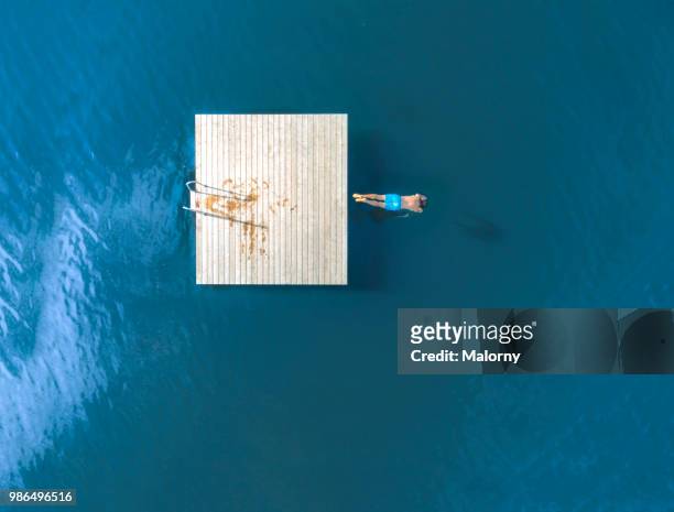 Man jumping from floating island into blue lake. Directly above, aerial view. Drone view.