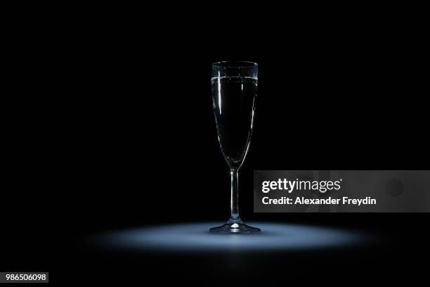 elegant glass with the transparent liquid on a black background on a white luminous spot - champagne flute transparent background stock pictures, royalty-free photos & images