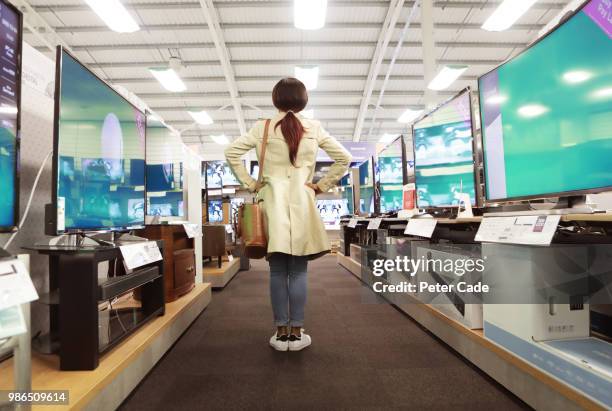 young woman in shop looking at televisions - appliance store stockfoto's en -beelden