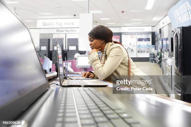 young woman in shop looking at laptops - generation z shopping stock pictures, royalty-free photos & images