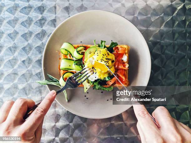 eating brunch with waffle, avocado, cucumber, salmon and poached egg, personal perspective - zalm gerecht stockfoto's en -beelden