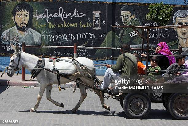 Palestinian family riding on a donkey-pulled cart pass in front of a mural depicting captured Israeli soldier Gilad Shalit and Ron Arad, an Israeli...