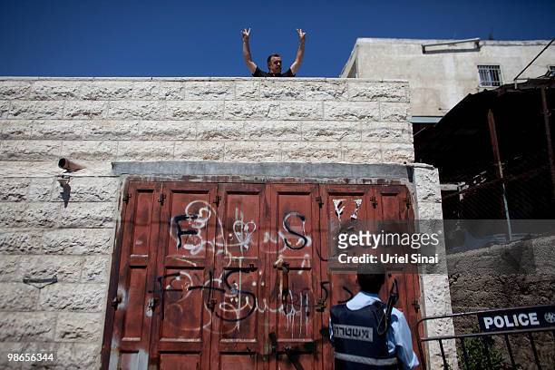 An Israeli policeman looks at an Arab man waving from his rooftop as right wing nationalist Israelis march through the Arab east Jerusalem...
