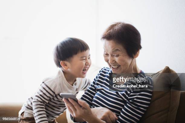 grossmutter und junge mit einem smartphone zusammen zu hause - asian granny pics stock-fotos und bilder
