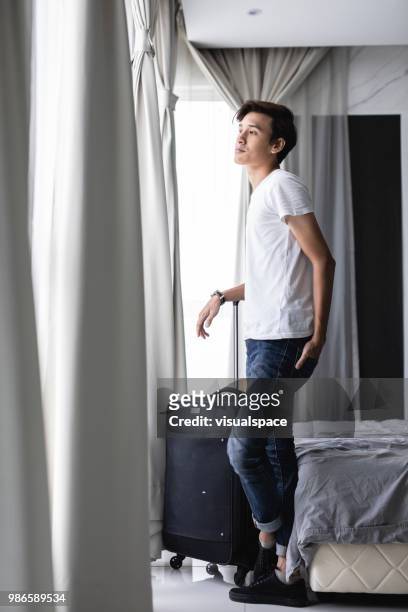 若い男の子は彼の隣にスーツケースをホテルの部屋に立っています。 - asain model men ストックフォトと��画像
