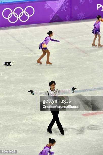 Yuzuru Hanyu from Japan celebrating while volunteers gather plush toys that Hanyu's fans threw onto the ice during the men's figure skating long...